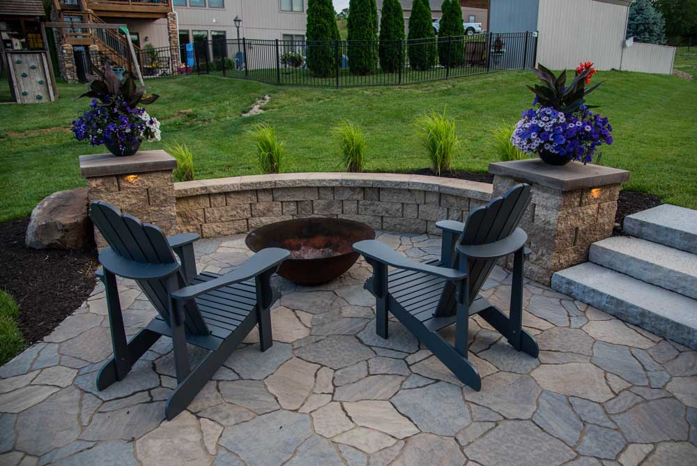 Paver patio featuring two Adirondack chairs, a fire pit, and landscaped flower arrangements, showcasing outdoor living design by Atlas Landscape.