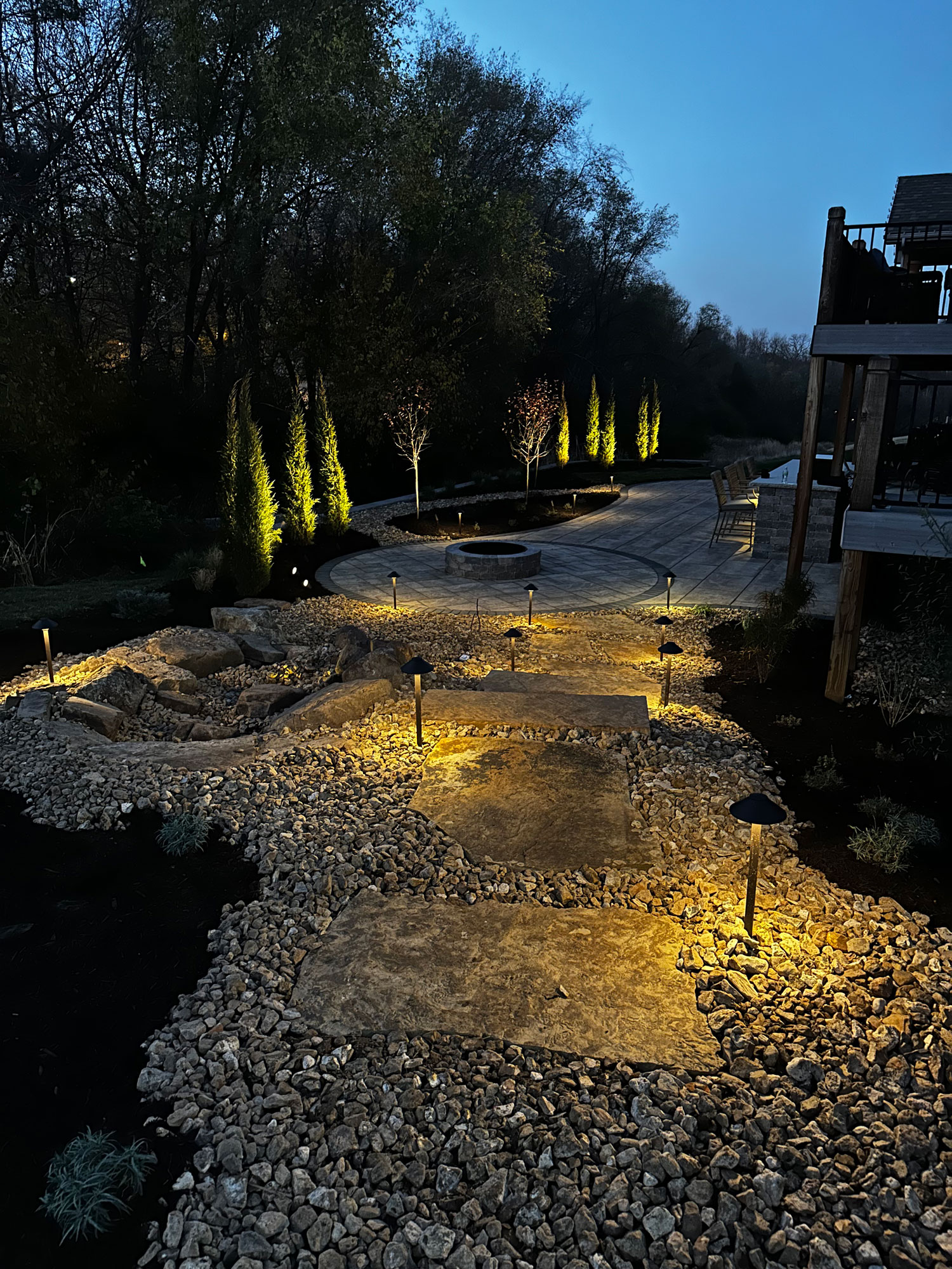 Landscape lighting illuminating stone pathway and garden features, enhancing outdoor ambiance at dusk, showcasing custom design by Atlas Landscape KC.