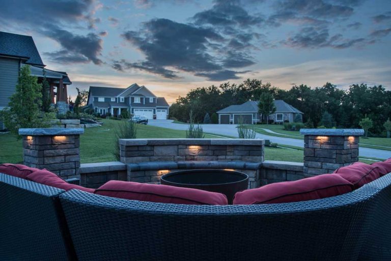 Stone fire pit seating area and landscape lighting at dusk