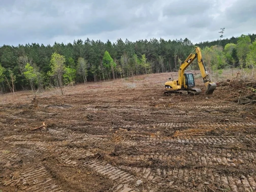 Excavator clearing wooded overgrowth and leaving bare ground and brush debris